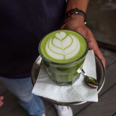 Warmer Matcha Latte im Glas mit Rosetta-Latte-Art, auf einem Tablett