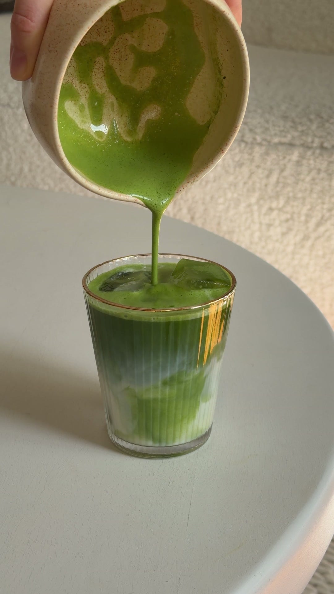 Matcha wird über Eis und Milch in ein Glas gegossen